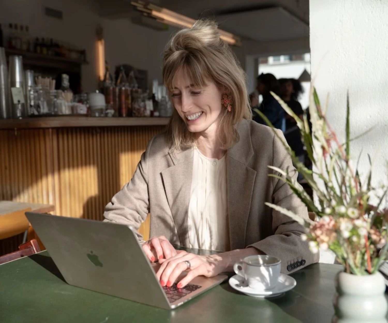 Frau arbeitet lächelnd an einem Laptop in heller Café- oder Büroumgebung.