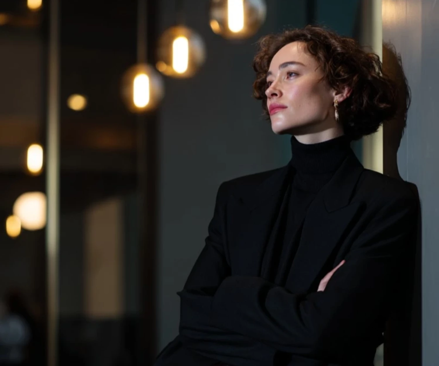 Porträt einer eleganten Frau mit langem schwarzen Haar, ernster Miene und schwarzem Rollkragenpullover, dunkler Hintergrund.